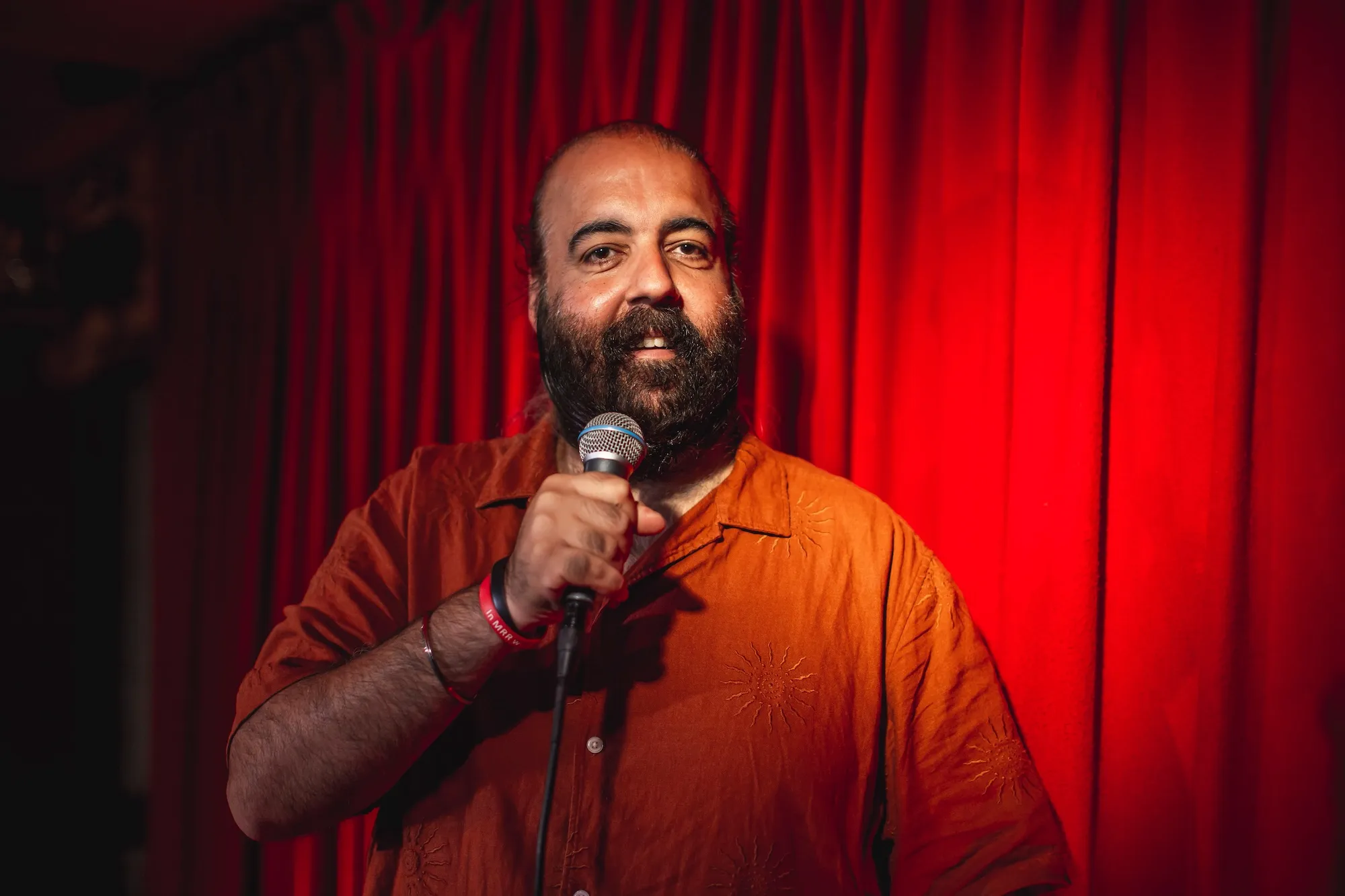 Standup comedian with microhphone in front of red curtains, Tallinn Fringe Festival 2026